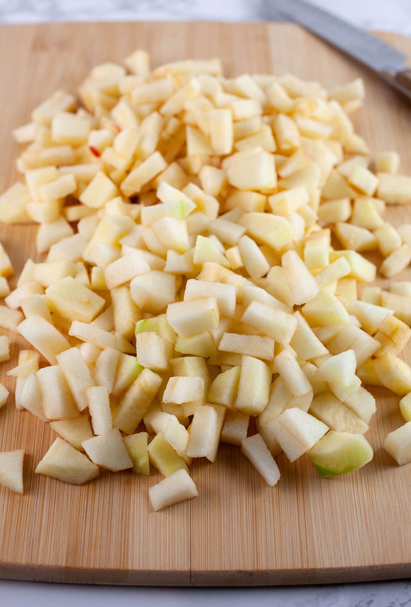 Chopped tart and sweet apples on wooden cutting board with knife.