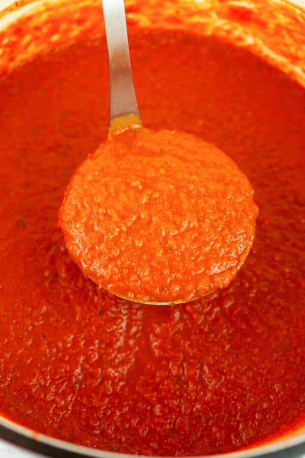Roasted tomato pasta sauce lifted from Dutch oven with metal ladle.