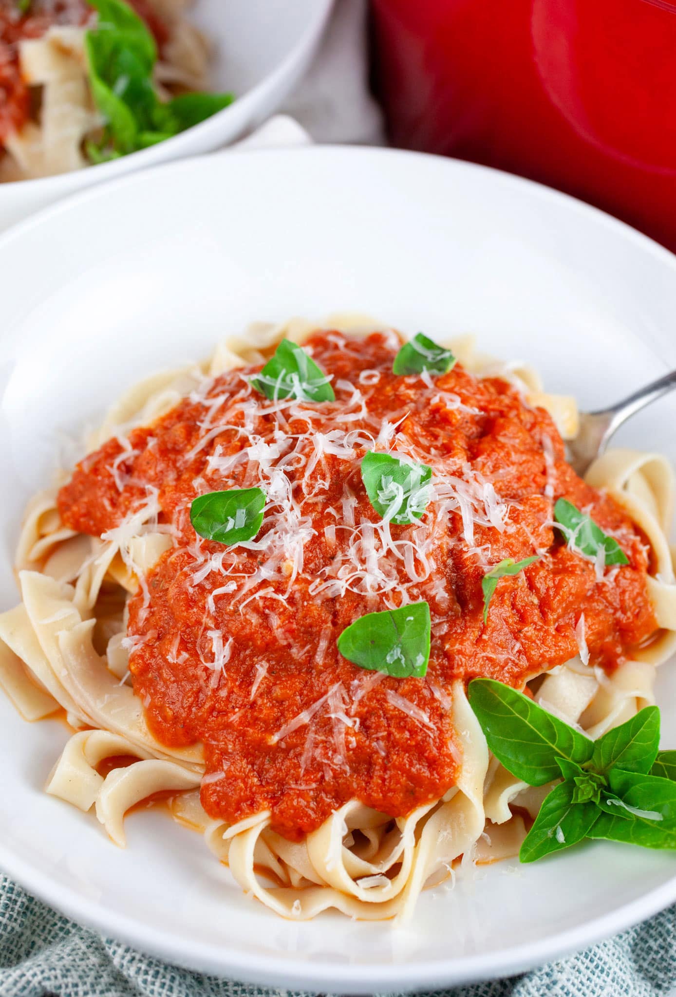 Roasted tomato pasta sauce in white bowl with fork garnished with grated Parmesan and fresh basil.