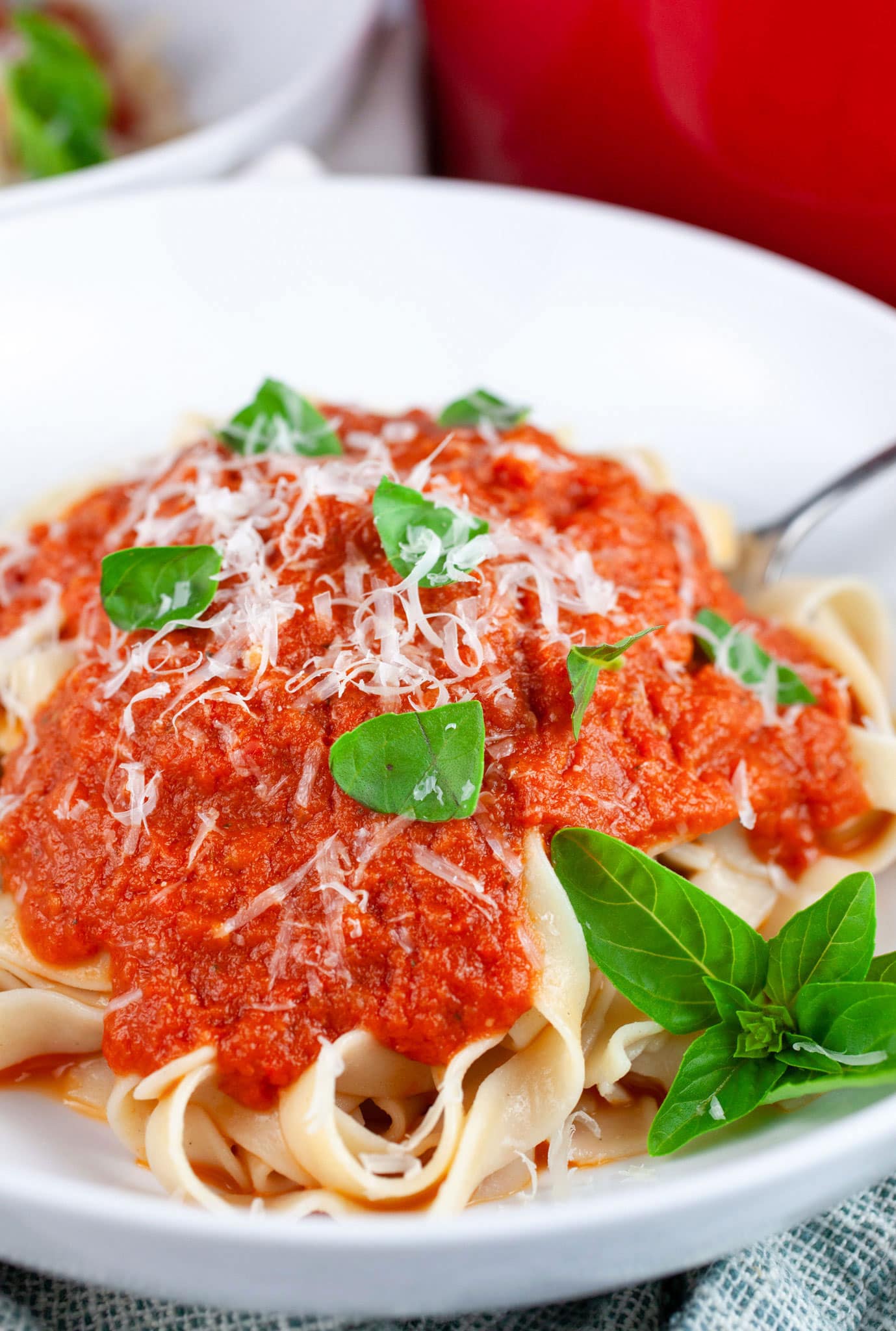 Roasted tomato pasta sauce on pappardelle garnished with grated Parmesan and fresh basil in white bowl with fork.