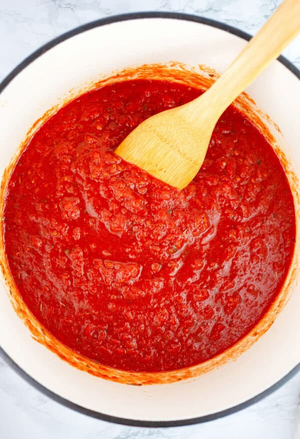 Crushed tomatoes cooking in Dutch oven with wooden spatula.