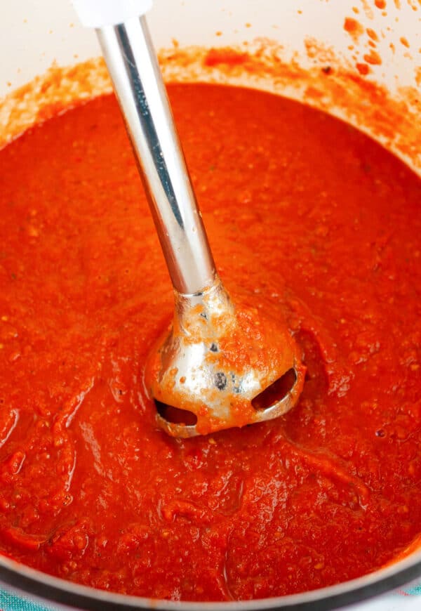 Immersion blender pureeing tomato sauce in Dutch oven.