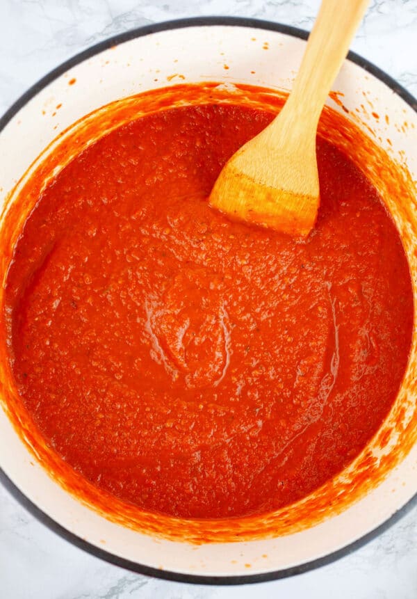 Cooked tomato sauce in Dutch oven with wooden spatula.