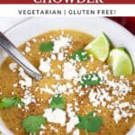 Southwest potato corn chowder garnished with Queso fresco, cilantro, and lime wedges in white bowl with spoon.