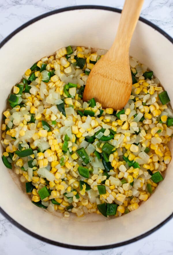 Garlic, onions, jalapeno and poblano peppers, and sweet corn kernels sauteed in Dutch oven with wooden spatula.