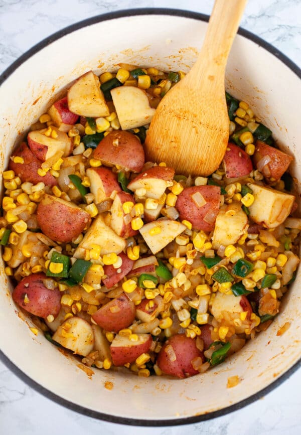 Garlic, onions, jalapeno and poblano peppers, sweet corn, and diced red potatoes sauteed in Dutch oven with wooden spatula.