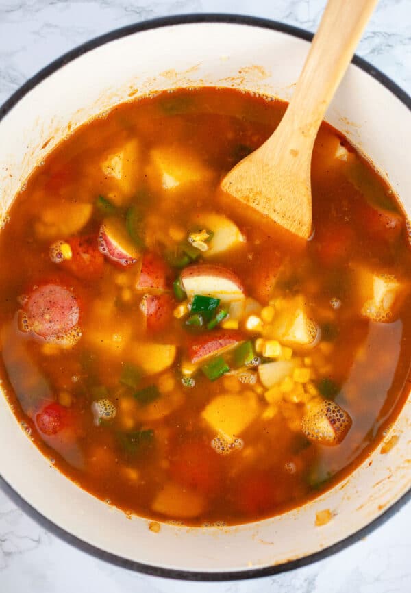 Uncooked Southwest potato corn chowder in Dutch oven with wooden spatula.