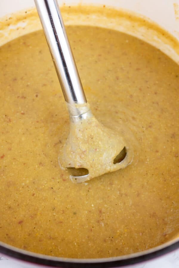 Immersion blender pureeing potato corn chowder in Dutch oven.
