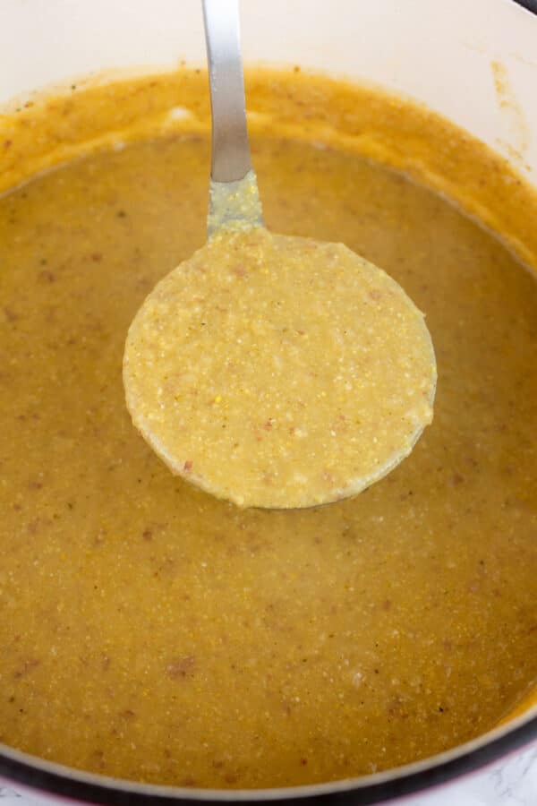 Scoop of corn potato chowder lifted from Dutch oven on metal ladle.
