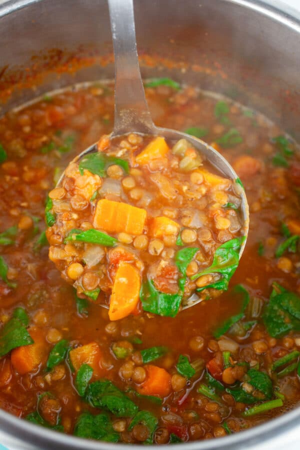 Metal ladle lifting scoop of lentil soup from Instant Pot.