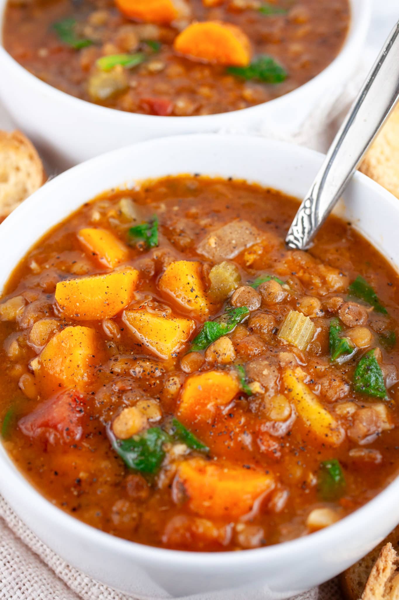 Lentil soup with carrots and spinach in white bowl with spoon.