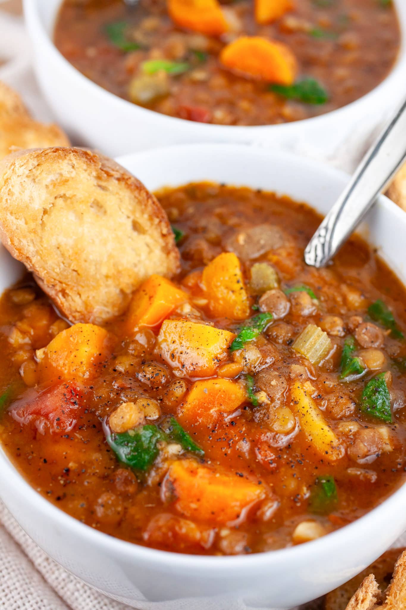 Instant Pot lentil soup with crostini in white bowl with spoon.