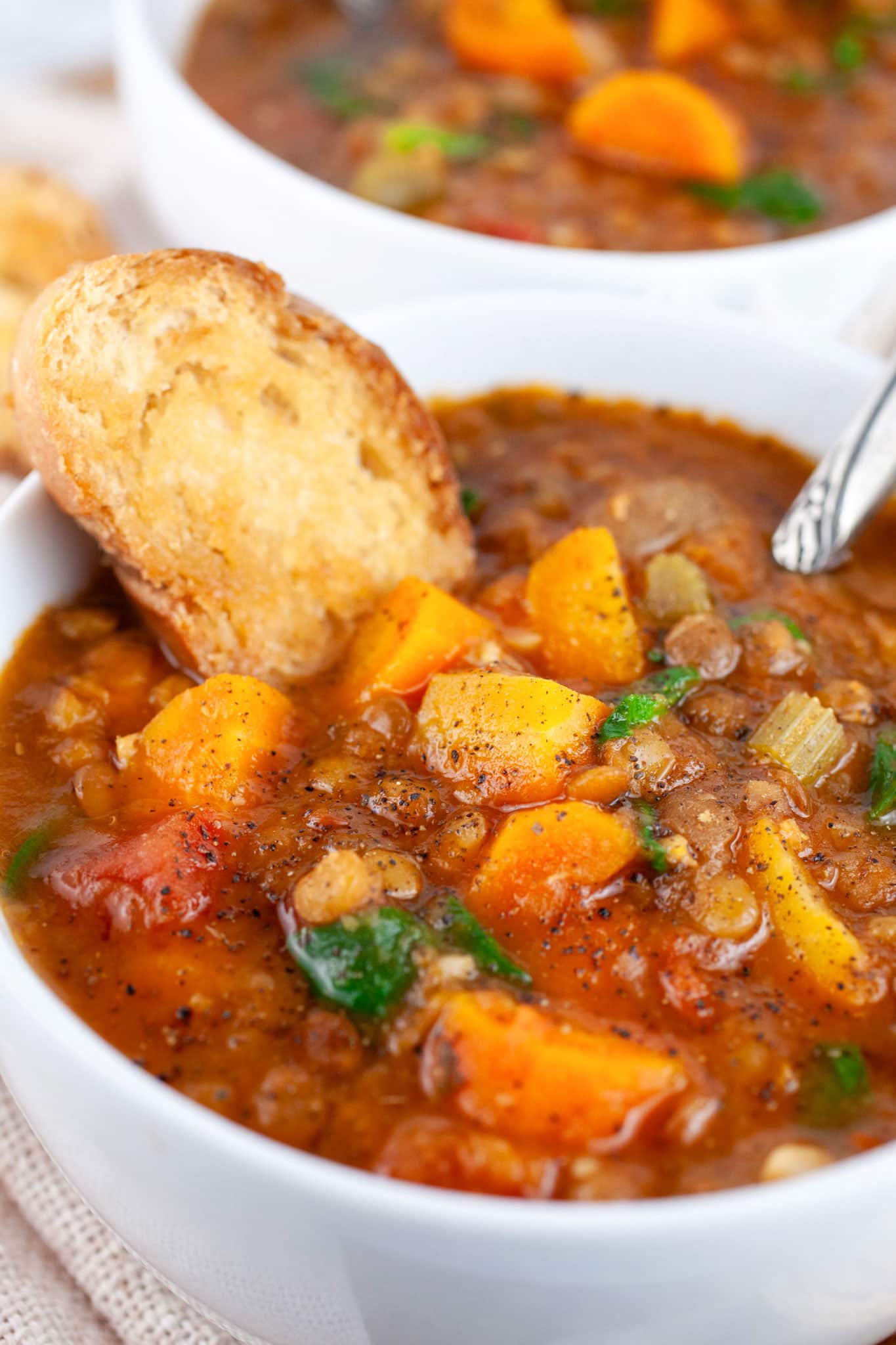 Instant Pot lentil soup with toasted crostini in white bowl with spoon.