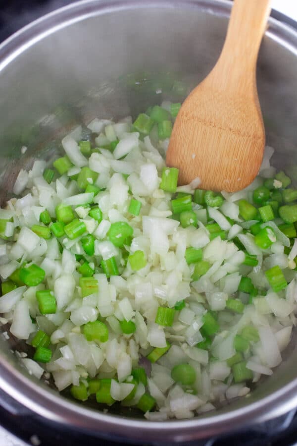 Minced garlic, onions, and celery sauteed in Instant Pot with wooden spatula.