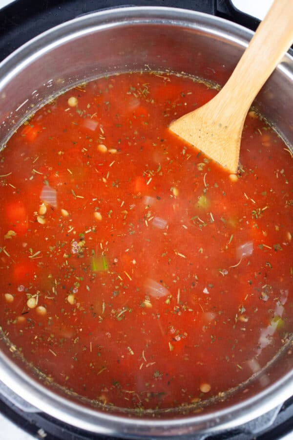Uncooked lentil soup in Instant Pot with wooden spatula.