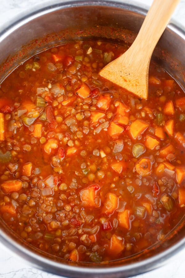 Cooked lentil soup in Instant Pot with wooden spatula.