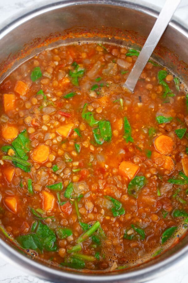 Lentil soup with spinach and carrots in Instant Pot with metal ladle.